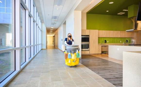 Janitorial service worker pushing cleaning cart through office hallway